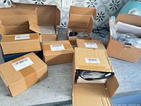 Seven cardboard boxes on tabletop, several open showing packing, barcodes visible