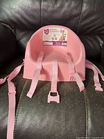 Front view of pink booster seat showing straps and buckle