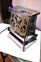 Front three-quarter view showing chrome body, cutout panels, Bakelite feet and cord connection