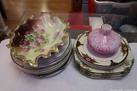Two stacks of porcelain luncheon plates, ruffled serving dish on left stack, pink art glass perfume bottle on right stack