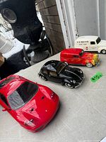 Four die cast cars grouped: red Ferrari coupe, black VW Beetle, red/yellow flame delivery car, white E.D. Smith's van
