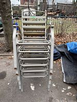 Front view of six stacked metal patio arm chairs showing slatted design and general wear