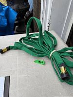 Entire green fabric garden hose coiled on table showing both brass-tone connectors