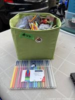 Green fabric cube full of assorted writing instruments with sealed Staedtler 16-colour fineliner set in front