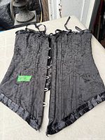 Full view of black jacquard corset showing front busk closure and ruffle trim