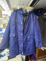 Front view of blue Northern Reflections winter coat hanging, showing buttons, zipper, pockets, hood with fur trim