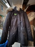 Front of black Vero Moda parka hanging, showing pockets, hood with fur trim