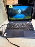 Laptop open, screen on at login, keyboard and trackpad visible, power adapter connected