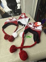 Three red and white knit earflap hats with tags displayed on table