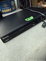 Front and top view of Philips black DVD player showing brand logo, disc tray and attached power cord