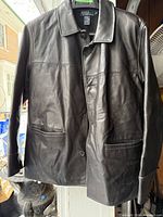 Front view of black leather jacket on hanger showing buttons, pockets, collar