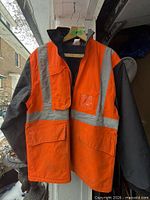 Front view of orange and black safety jacket with reflective stripes and pockets