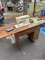 Full view of sewing machine mounted in cabinet with accessories on top