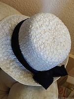 Top and side view of white woven straw hat with black ribbon and bow