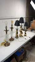 Five table lamps on table: two pressed glass & brass, three gold sculptural with black shades