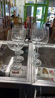 Five clear stemmed wine glasses on glass display case
