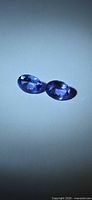 Two oval blue-violet faceted tanzanites on neutral background