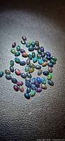 Pile of small multicoloured opal cabochons on black background