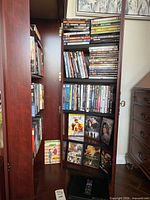 Open wooden media cabinet showing multiple shelves filled with DVD cases and a black DVD player at the bottom