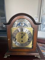 Front view of wood mantel clock showing dial, moon phase and brass feet