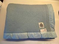 Folded baby blue wool blanket showing Woolmark tag and satin trim
