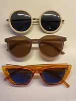 Front view of three sunglasses stacked: cream round, brown round, orange cat-eye