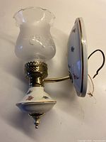 Full view of ceramic and brass sconce with frosted glass shade attached