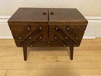 Front view of closed wooden accordion sewing box on legs