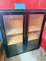Front view of black cabinet showing doors, red handles and shelves behind textured panels