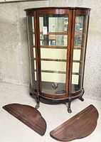 Full view of oak bow-front curio cabinet with two shelves on floor