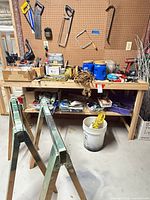 Workbench with tools, sawhorses in foreground, buckets and extension cord on floor