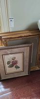 Two ornate gilt frames and one silver-grey framed botanical print leaning against wall