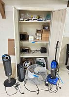 Full view of open beige metal cabinet and small appliances on floor