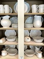 Cabinet close-up showing mugs, pierced plates, pitchers, stacked plates and serving bowls