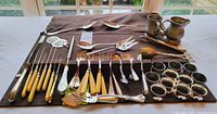Full lot overview showing flatware, napkin rings and pewter pitchers on cloth mat