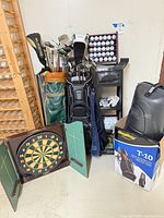 Overall lot showing golf bags, clubs, ball rack, dartboard, BagBoy T-10 box and hard case