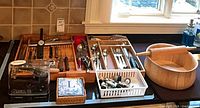Counter view showing wooden bowl, rolling pin, utensil trays with knives, flatware, kitchen tools, lever corkscrew set, napkins