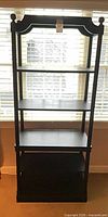 Full frontal view of tall black bookcase showing five shelves and decorative top