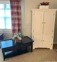white armoire beside dark coffee table with floral arrangements