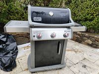 Front view of Weber Spirit 3-burner grill showing lid, control panel, side shelves, cover on ground