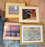 Four framed artworks grouped on carpet: seascape, desert arch, Nile sunset, world map
