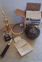 Group view of bowling ball, box, tennis racket, trophies and documents