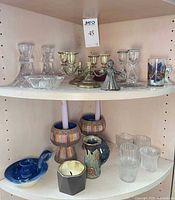 Shelf with assorted glass, brass, pewter and ceramic candle holders