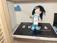 Front view of rag doll standing on Ouija board game box