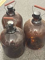 Three amber glass carboy jugs grouped together showing overall form, caps, and handles