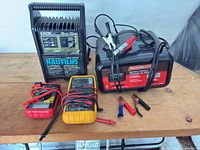 Group view of Exide charger, MotoMaster charger, Fluke meter, generic meter, clamp leads
