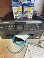 Printer with ink boxes on top, blue network cable and manual shown