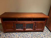 Front view of wood entertainment cabinet showing four doors, glass panels on center doors, three upper shelves