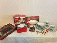 Full lot view showing boxed platter, boxed mugs, dinnerware stacks, accessories, placemats