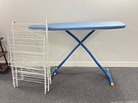 Ironing board standing with three drying racks folded beside it
